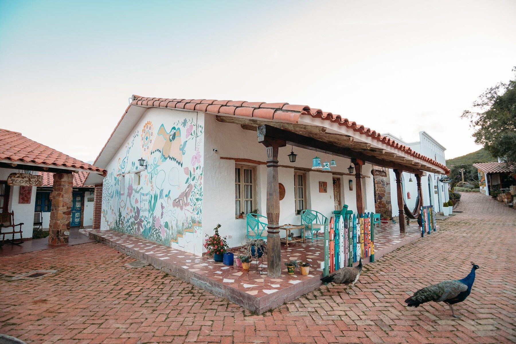 A tiled-roof casita at El Pueblito, painted mural on the gable, peacocks on the brick path outside