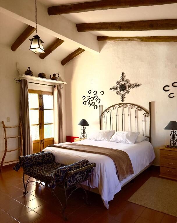 A guest room at El Pueblito, beamed ceiling, iron bedstead and a shuttered window