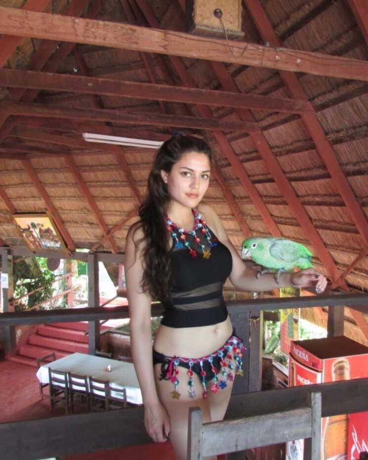 Charlene Amini under a thatched roof in Riberalta, a green parrot on her hand