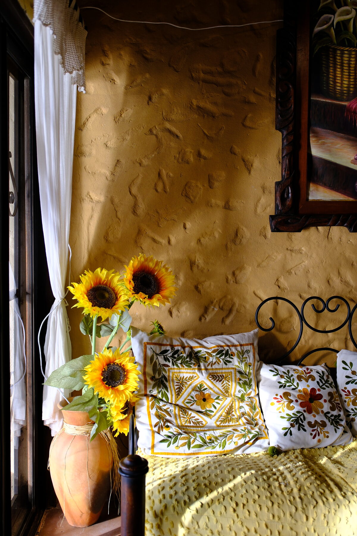 Sunflowers in a clay jug beside an embroidered bed