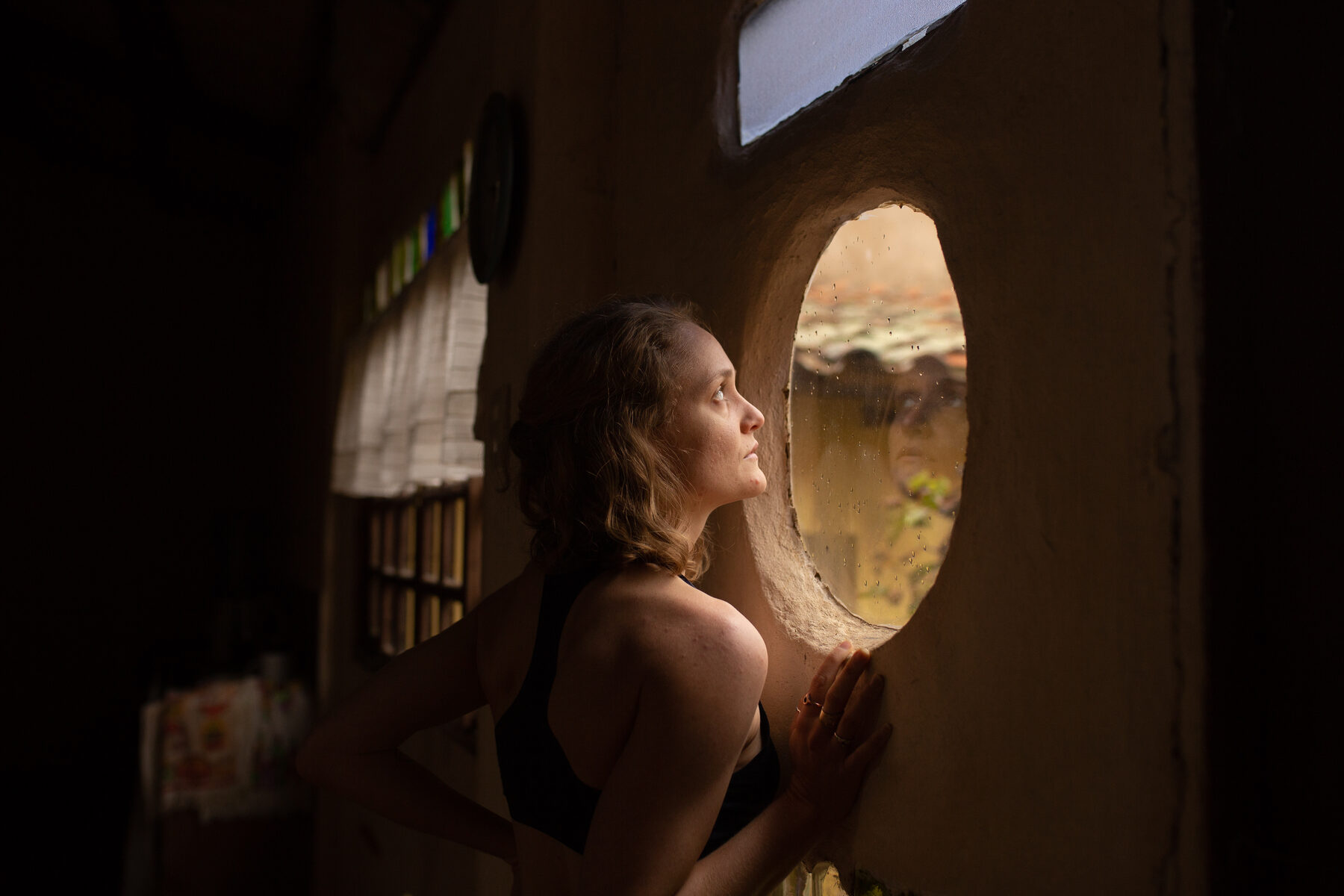 A guest resting at a round window, late light on the wall